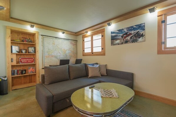 A living room with a sofa, a coffee table, a bookshelf, a map, and a painting.