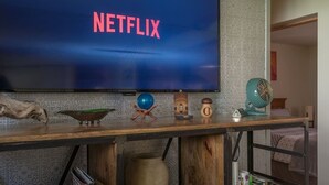 Et fjernsyn der viser Netflix-logoet, en træhylde med diverse pyntegjenstande, og en væg med et mønster.