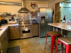 A modern kitchen with stainless steel appliances, a microwave, a stove, and a refrigerator. There are two red stools and a wooden bar counter.
