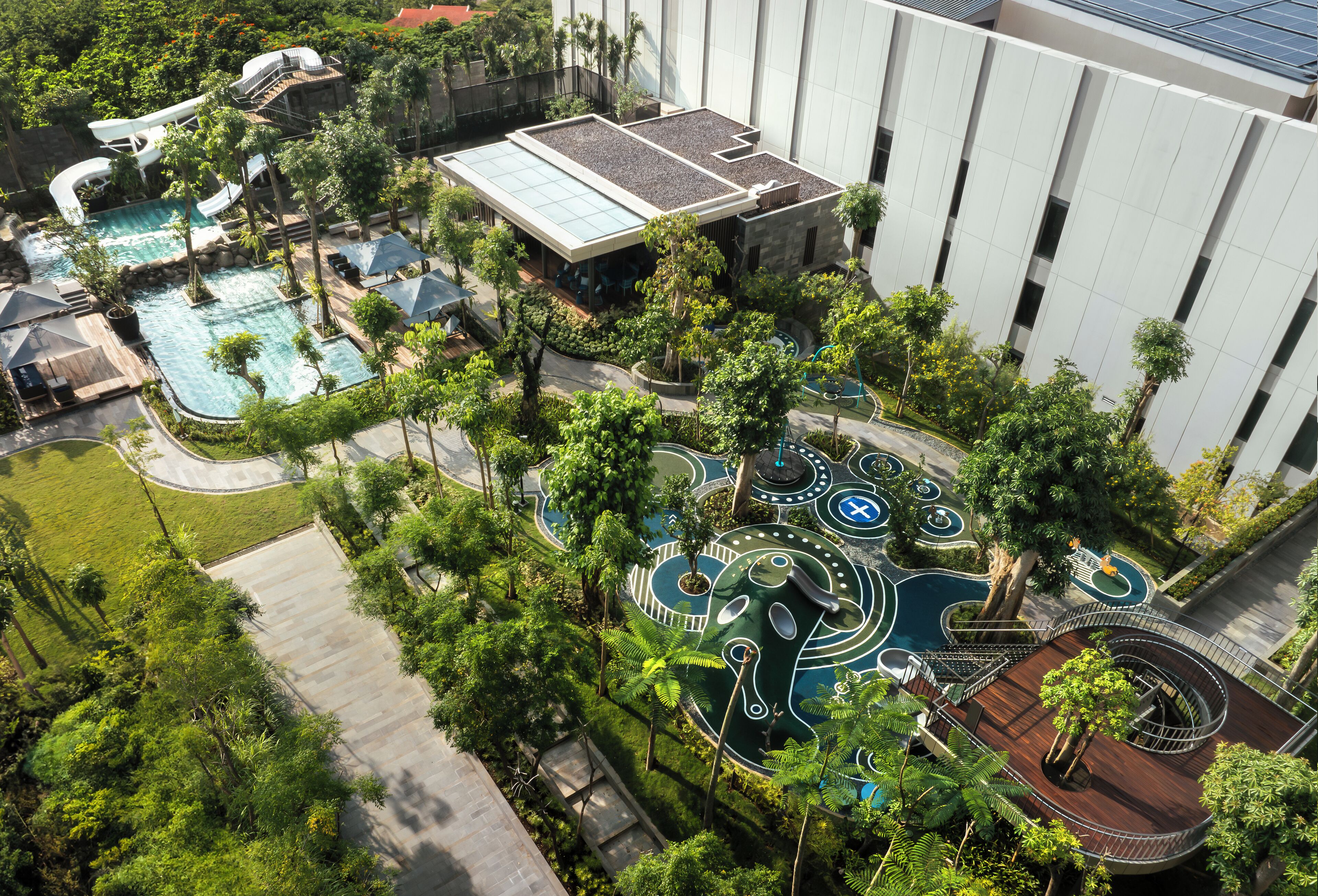 An aerial view of a resort with multiple swimming pools, a water slide, and a playground area surrounded by lush greenery.