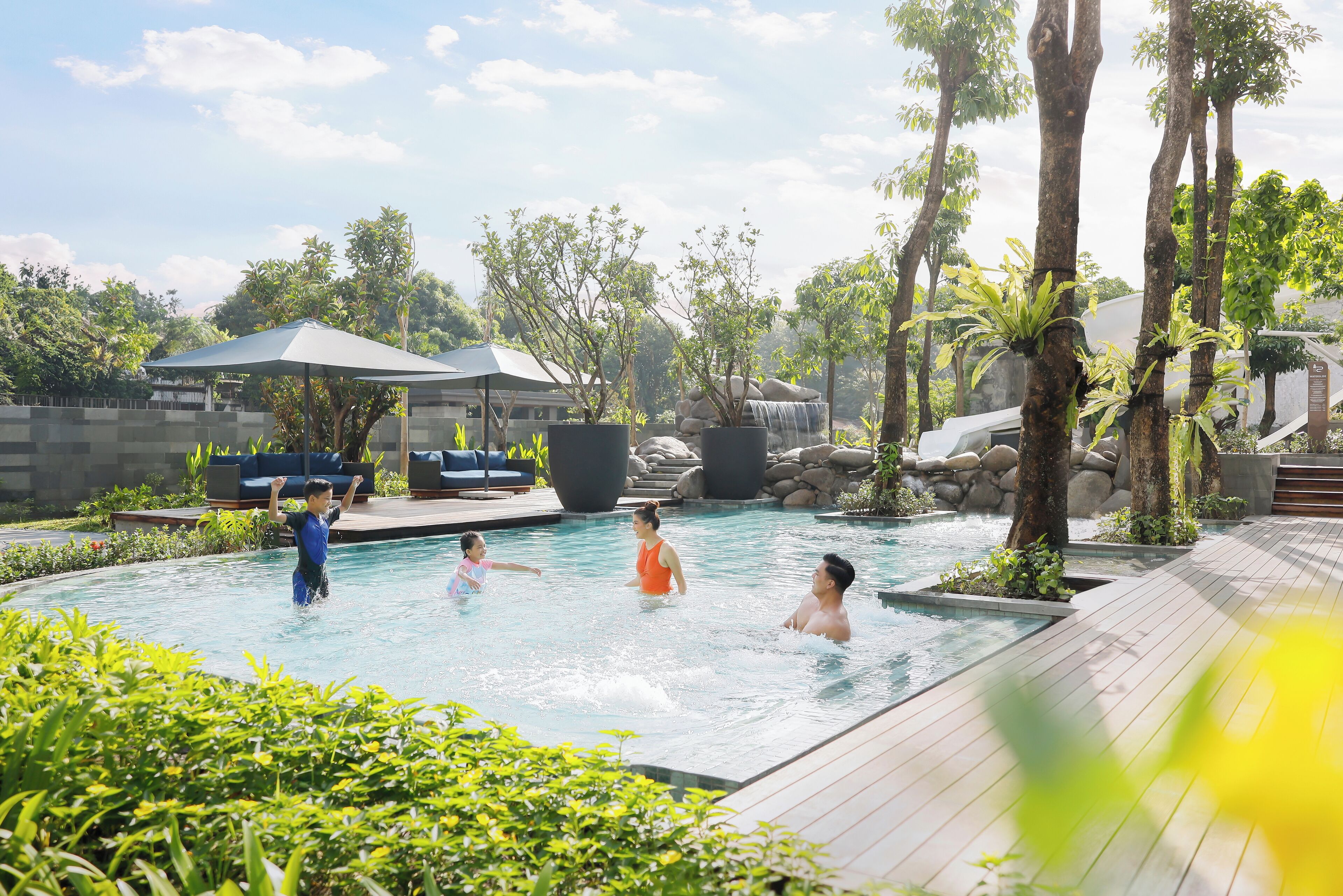 A pool area with a wooden deck, lounge chairs, and a waterfall feature.