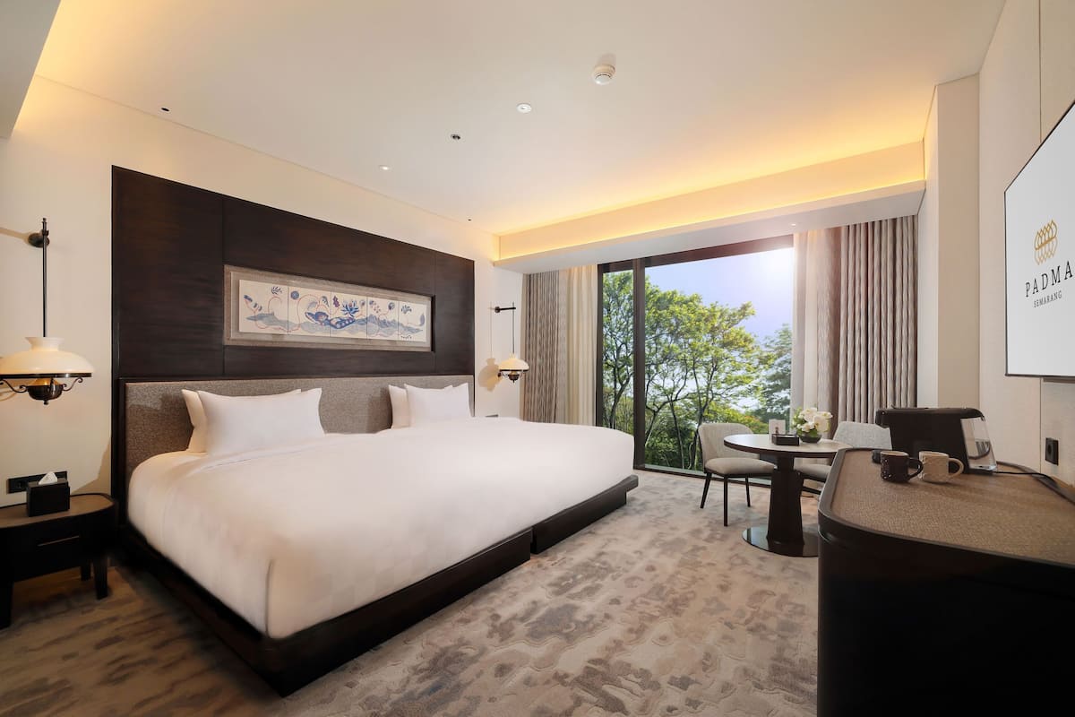 A modern hotel room with a large bed, a desk, and a view of the outdoors.