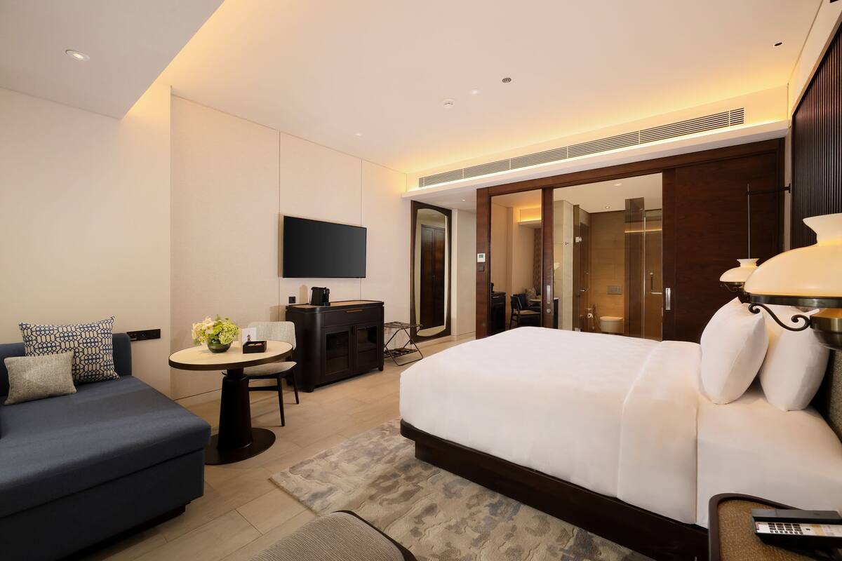 A modern hotel room with a large bed, a sofa, a desk, and a TV.