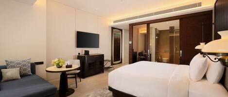 A modern hotel room with a large bed, a sofa, a desk, and a TV.