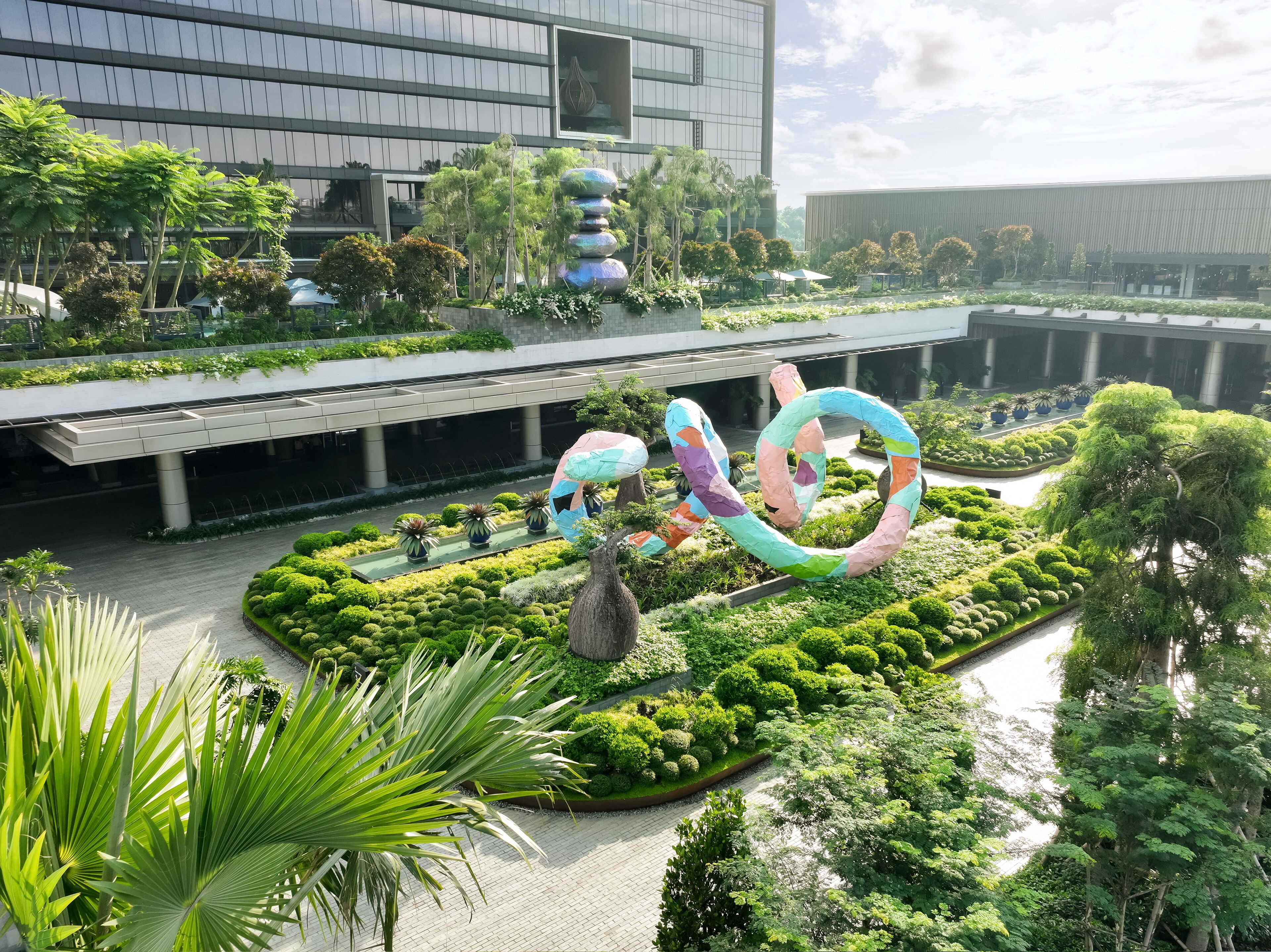 A landscaped area with a central sculpture, surrounded by neatly trimmed bushes and trees.