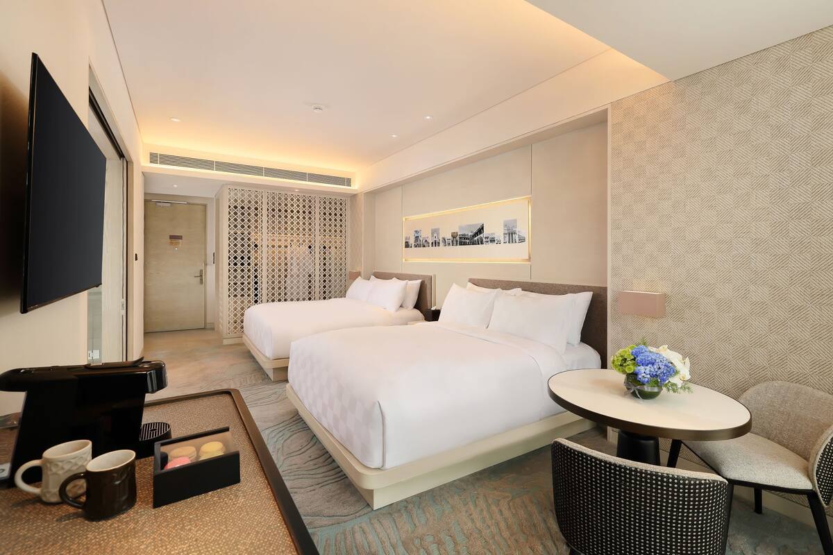 A hotel room with two beds, a TV, a coffee maker, and a small table with a flower arrangement.