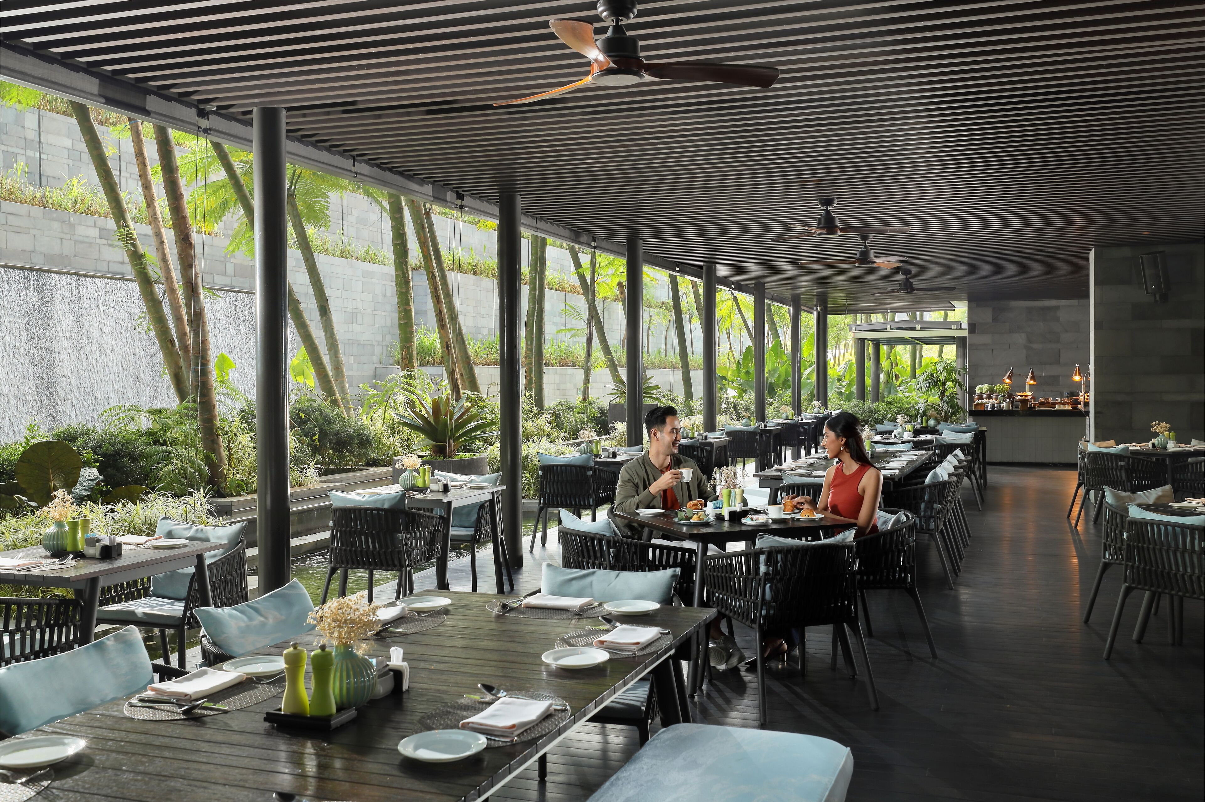 A restaurant with outdoor seating, large windows, and a waterfall view.