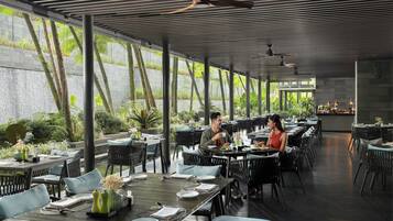 Un restaurante con terraza, amplios ventanales y vistas a una cascada.
