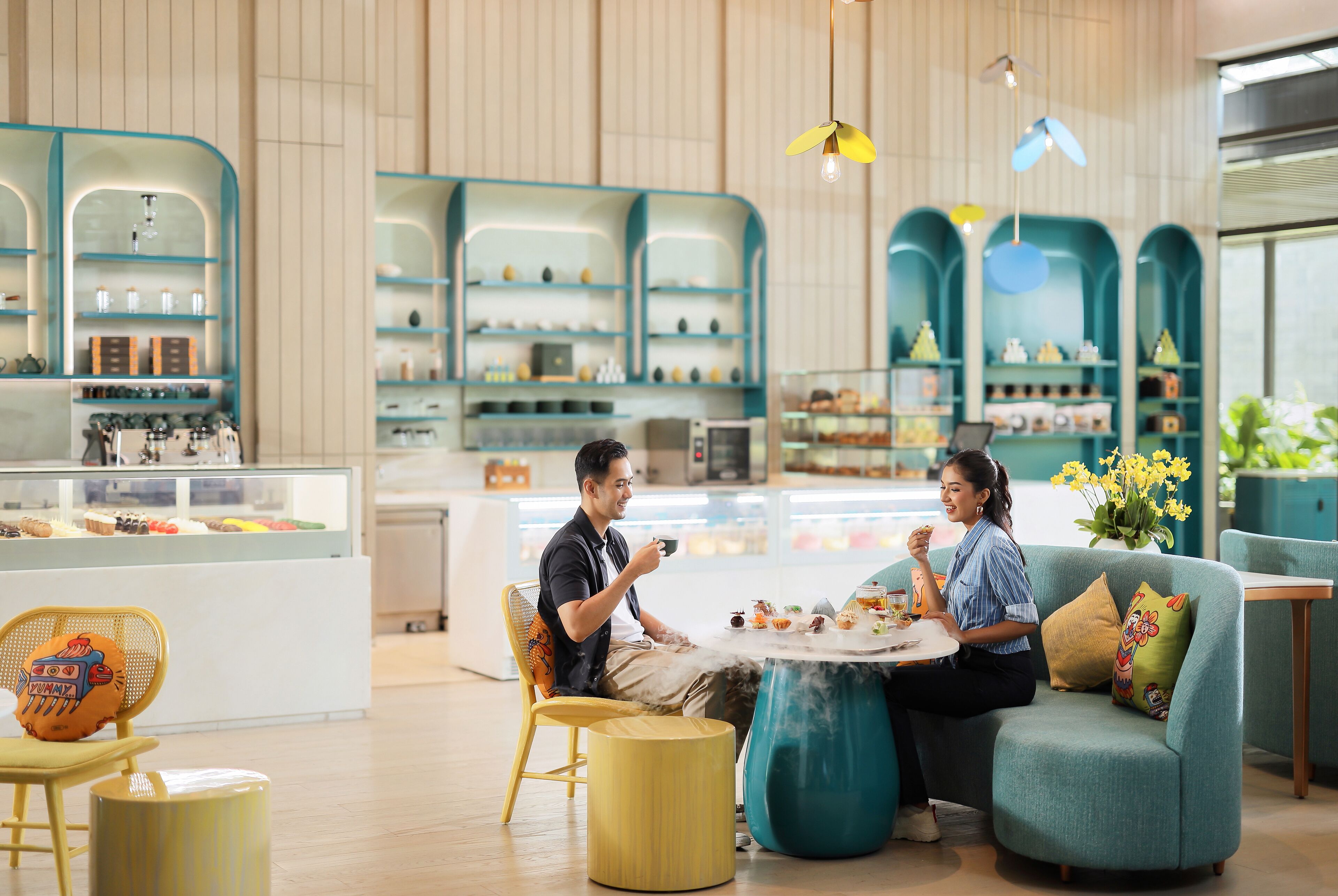 L’intérieur d’un café moderne, avec des espaces aménagés pour s’asseoir, un comptoir où sont exposées des pâtisseries et des éléments décoratifs.