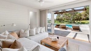 Un moderno salón con sofá, una mesa de centro y vistas a una piscina y jardín.