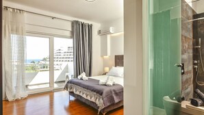 Una habitación de hotel moderna con una cama grande, cabina de ducha de vidrio y un balcón con vistas a la ciudad.