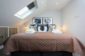 Quarto com uma cama grande, um claraboia, duas obras de arte emolduradas e um guarda-roupa.