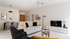 A modern living room with a sofa, two armchairs, a coffee table, a dining area with chairs, a TV, and artwork on the walls. - Top-Class 2BR Apartment in Marousi (Marousi)