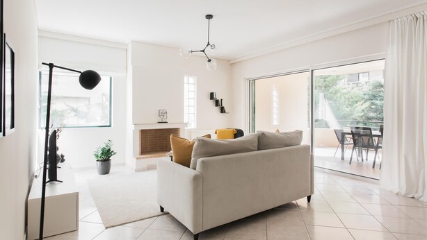 A modern living room with a sofa, a fireplace, a dining area, and a large sliding glass door to the outdoors. - Top-Class 2BR Apartment in Marousi (Marousi)
