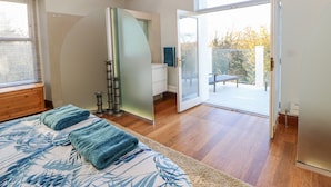 A bedroom with a bed, a large mirror, a wooden ceiling beam, and a sliding glass door leading to an outdoor deck.