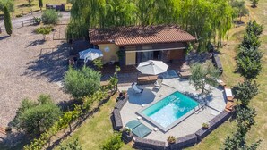 An aerial view of a house with a swimming pool, surrounded by trees and a garden.