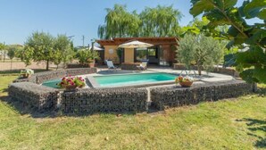 A pool surrounded by stone walls, a covered seating area, and various plants.