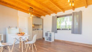 A modern, open-plan living space with a wooden ceiling, a dining area with a table and chairs, a kitchen, and a large window with curtains.
