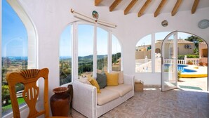 A spacious room with a white sofa, a wooden chair, and a large window offering a view of the countryside. - Castellons Vida by Interhome (Moraira)