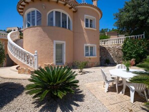 Une maison à deux étages dotée d’une façade incurvée, d’un escalier en colimaçon et d’un patio aménagé avec du mobilier d’extérieur.