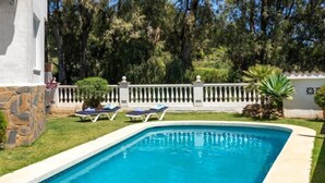 A rectangular swimming pool with a stone wall on one side and a white fence in the background. - Villa Juna by Interhome (Benalmádena Costa)