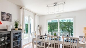 A bright dining area with a table and chairs, a cabinet with glass doors, a Buddha painting, and a view of greenery outside. - Massenet by Interhome (Saint Aygulf)