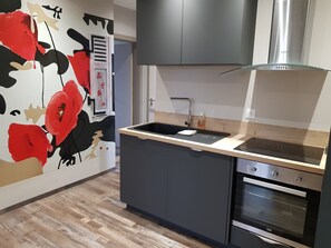 A modern kitchen with a black countertop, stainless steel appliances, and a wooden floor.