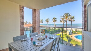 A balcony with a table set for dining, overlooking a pool and palm trees, with a clear view of the beach. - Beautiful apartment in First Line Marina Azul (Els Poblets)