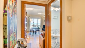 A hallway leading to a dining area with a view of the sea, a bathroom with a tiled sink, and a colorful wall with abstract art. - Beautiful apartment in First Line Marina Azul (Els Poblets)