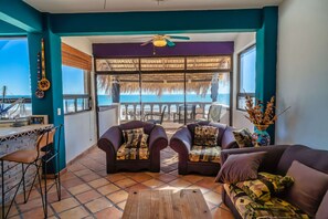 A room with a view of the sea, featuring two sofas, a wooden table, and a bar area with a chair.