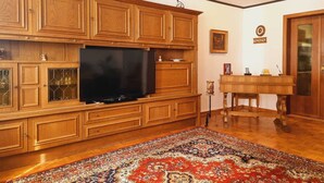 Una sala de estar con un mueble grande de madera para entretenimiento, un televisor de pantalla plana, una alfombra estampada y una mesita con una lámpara.