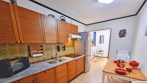 Una cocina compacta con armarios de madera, un microondas integrado y una zona de comedor con una mesa dispuesta para cuatro.