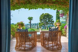 Wicker chairs with cushions facing a scenic view of a town and mountains. - Sea View Villa with Pool (Vallauris)