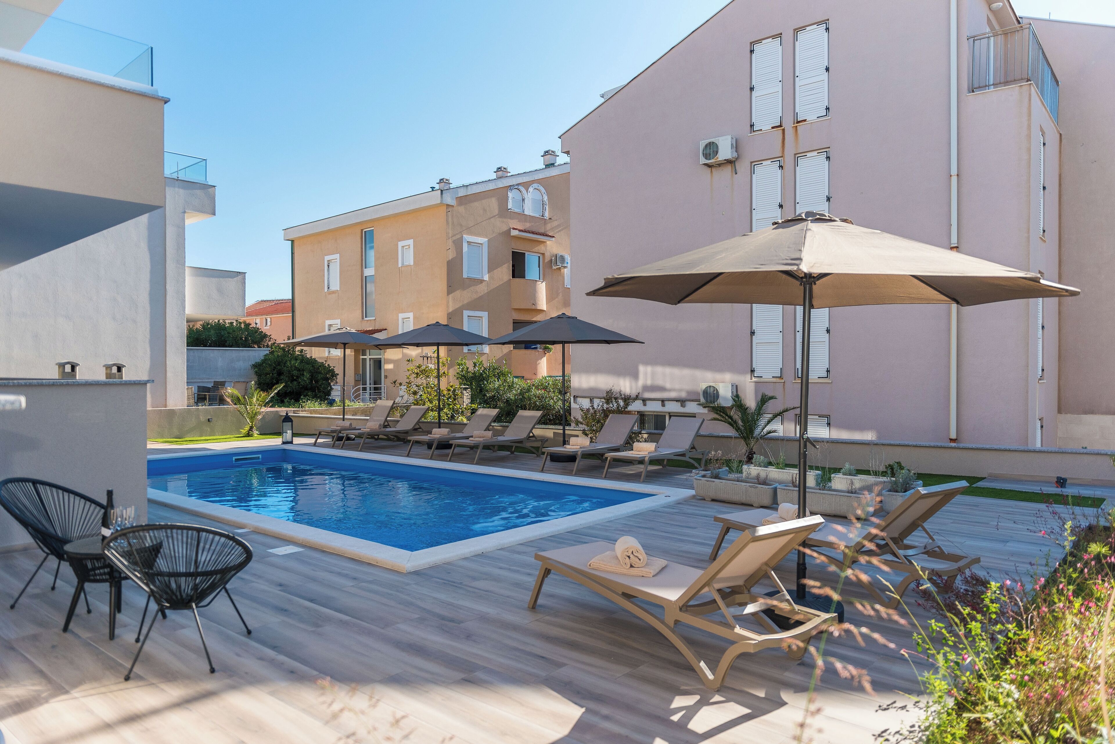 Zona de piscina con sillones reclinables, sombrillas y una alberca.