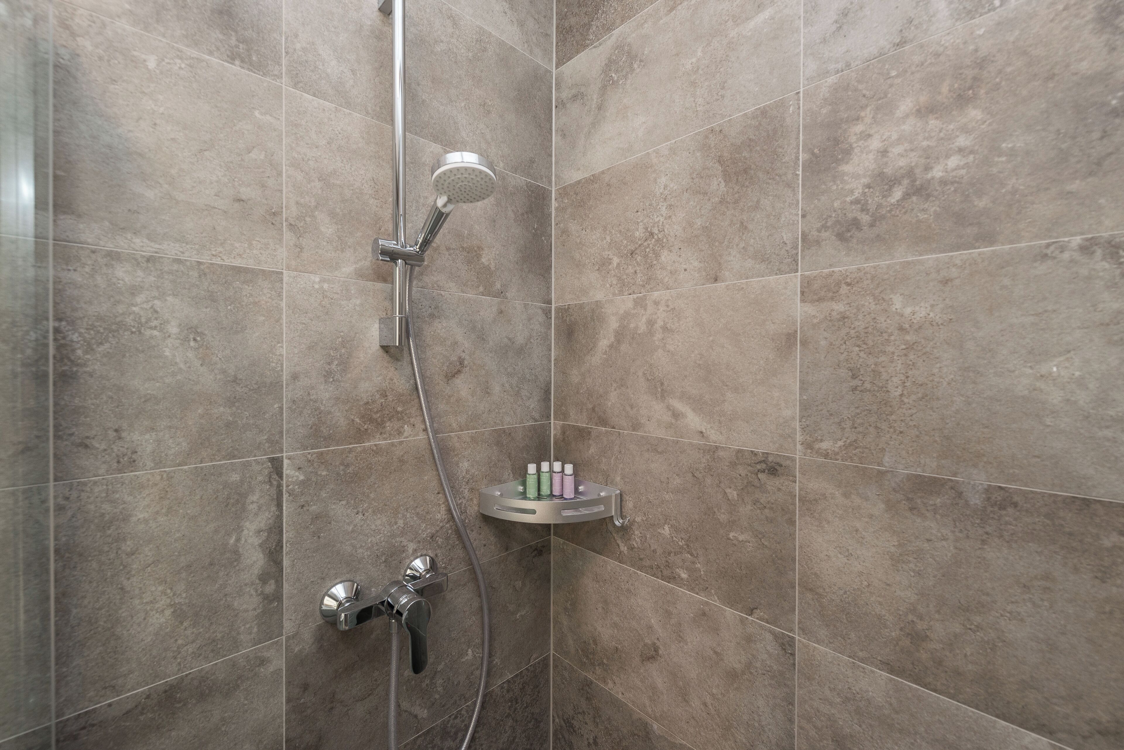 A shower with a handheld showerhead, a wall-mounted faucet, and a shelf with toiletries.