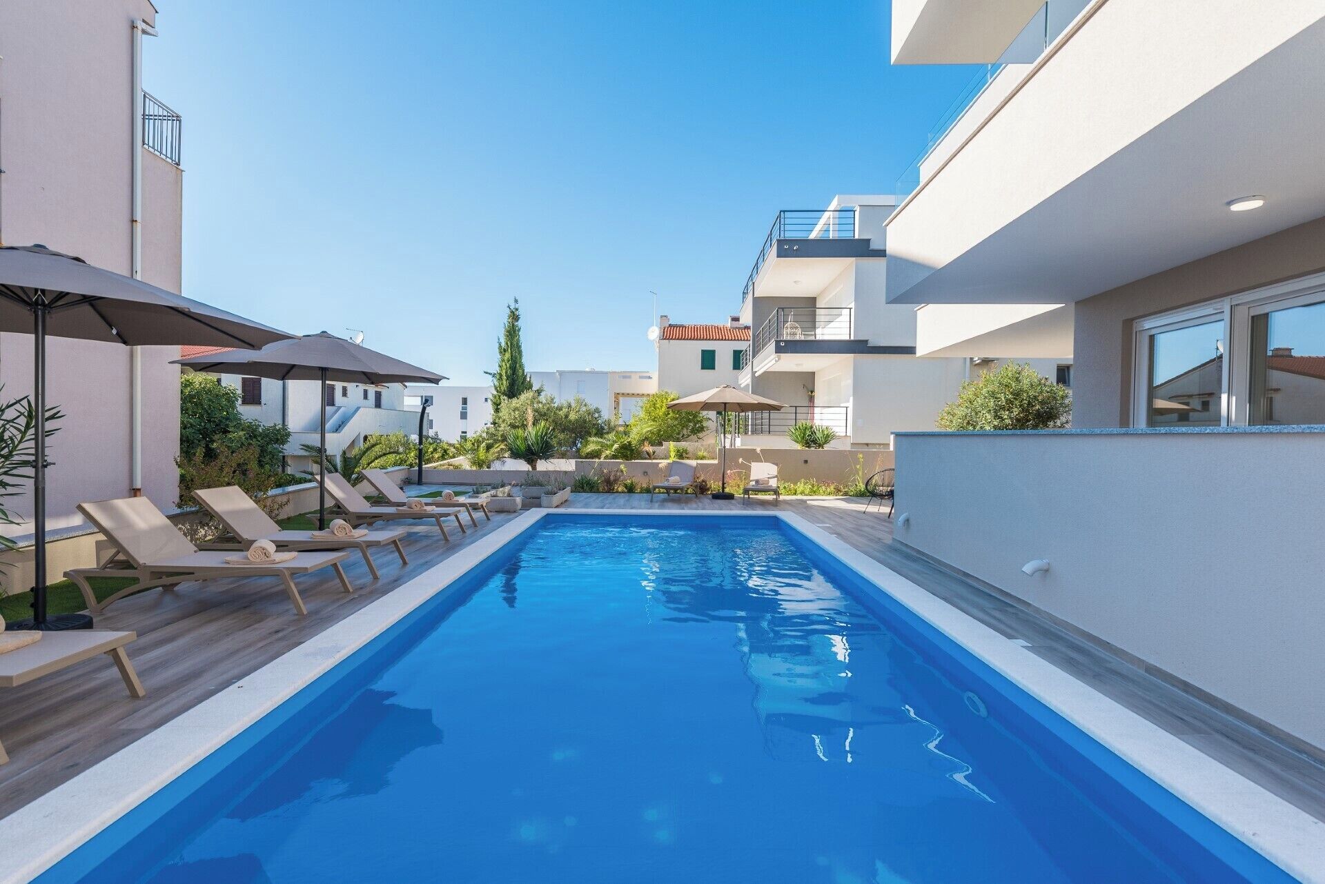 Piscina com espreguiçadeiras e guarda-sóis, rodeada por edifícios modernos.