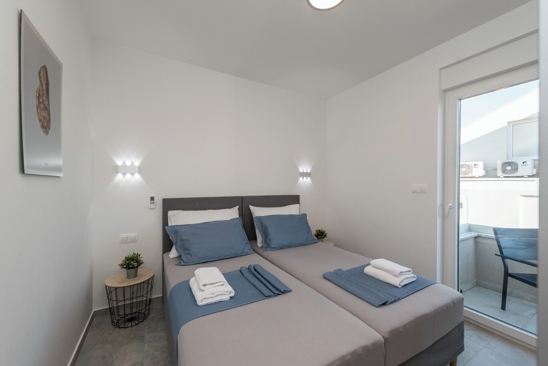 Una habitación de hotel moderna con dos camas, una mesita auxiliar con una planta y un balcón con una silla.