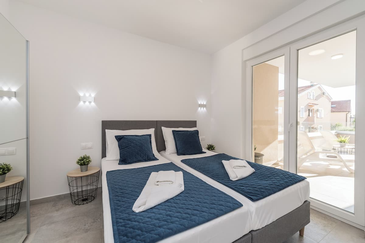 A modern hotel room with two beds, a balcony, and a view of the city.