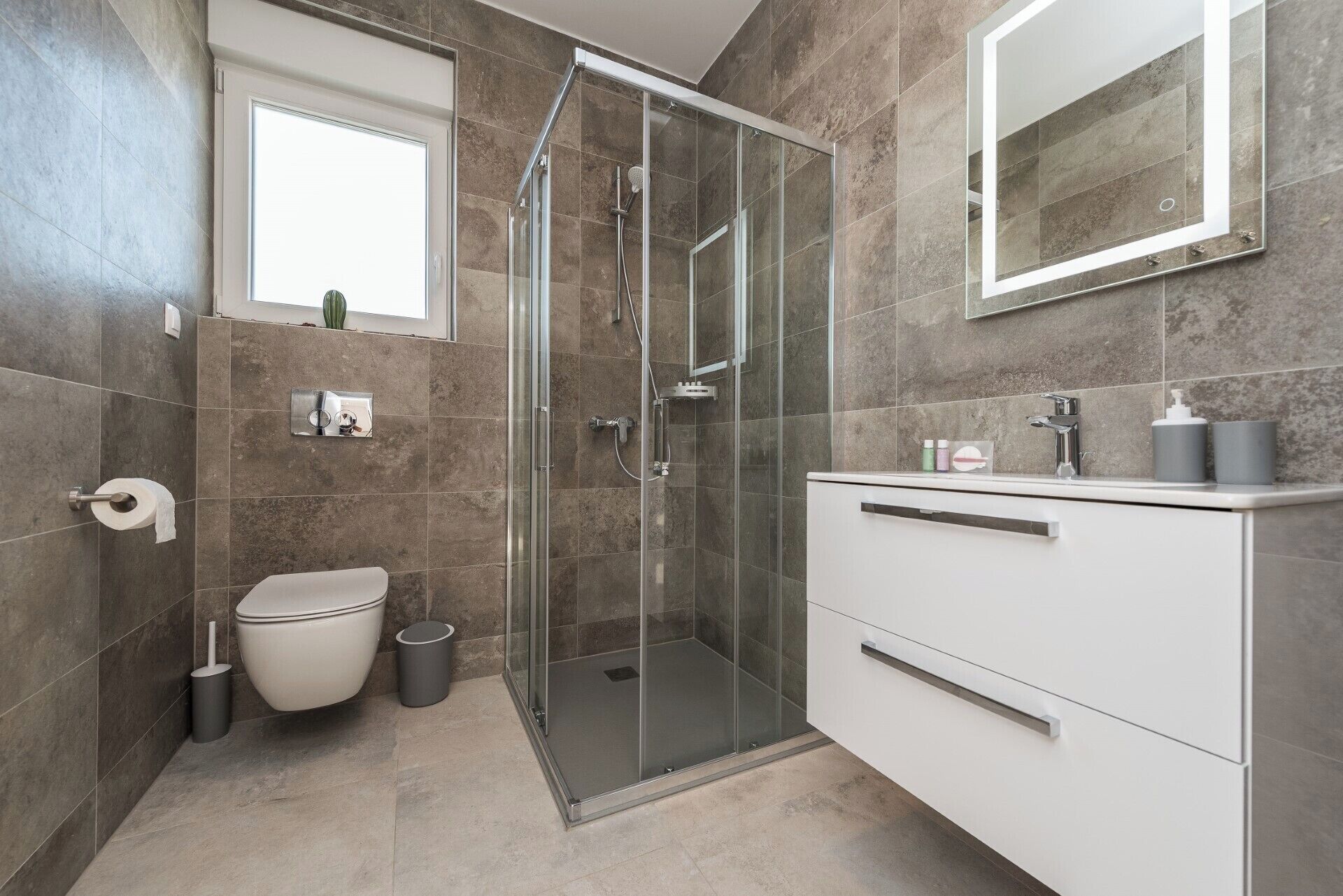A modern bathroom with a glass-enclosed shower, a toilet, and a vanity with a mirror.
