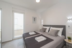 A modern bedroom with two beds, a sliding glass door, a bedside table with a plant, and a wall-mounted light fixture. - Pool apartments Villa Meteorite (Novalja)