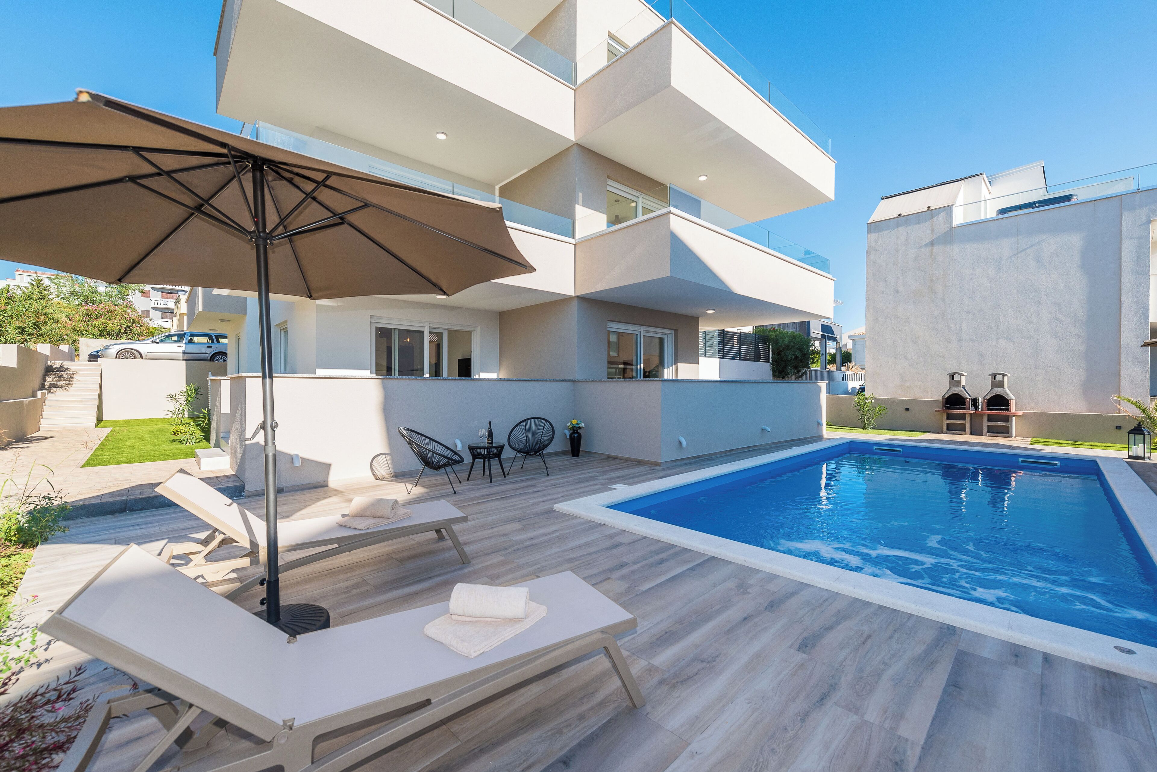 Ein moderner Poolbereich im Freien mit einem geometrisch gestalteten Pool, Liegestühlen und einer Pergola.