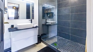 Un baño moderno con cabina de ducha de vidrio, un lavabo blanco y un espejo grande.