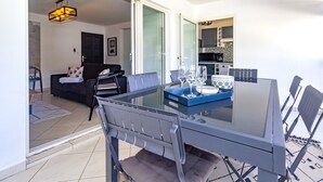 Un salón moderno con una mesa de comedor de cristal, sillas tapizadas en gris, un sofá y una cocina al fondo.