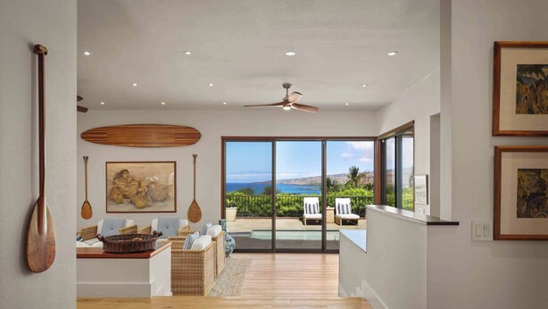 Uma sala espaçosa com vista para o oceano, um ventilador de teto e um espaço de refeições com mesa e cadeiras de vime.