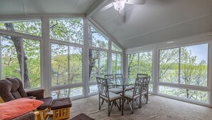 A sunroom with large windows, a ceiling fan, and a dining area with chairs and a table.