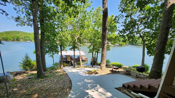 A lakeside deck with a grill, a covered area, and a view of the lake.
