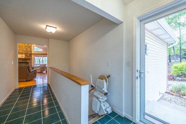 A hallway with a tiled floor, a wooden handrail, a white toilet, and a door leading outside.