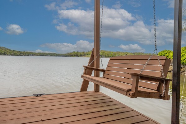 A wooden swing chair on a dock with a view of a calm lake and distant hills. - Whispering Winds - Great House on a Great Point (Camdenton)
