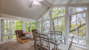 A sunroom with large windows, a ceiling fan, and a dining table with chairs.