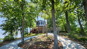 A modern house with a curved driveway, surrounded by trees and a stone retaining wall.